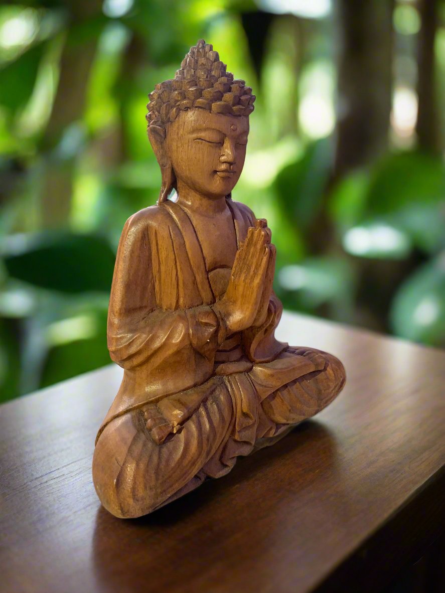 Wooden Buddha statue in meditation with hands in prayer on a wooden surface