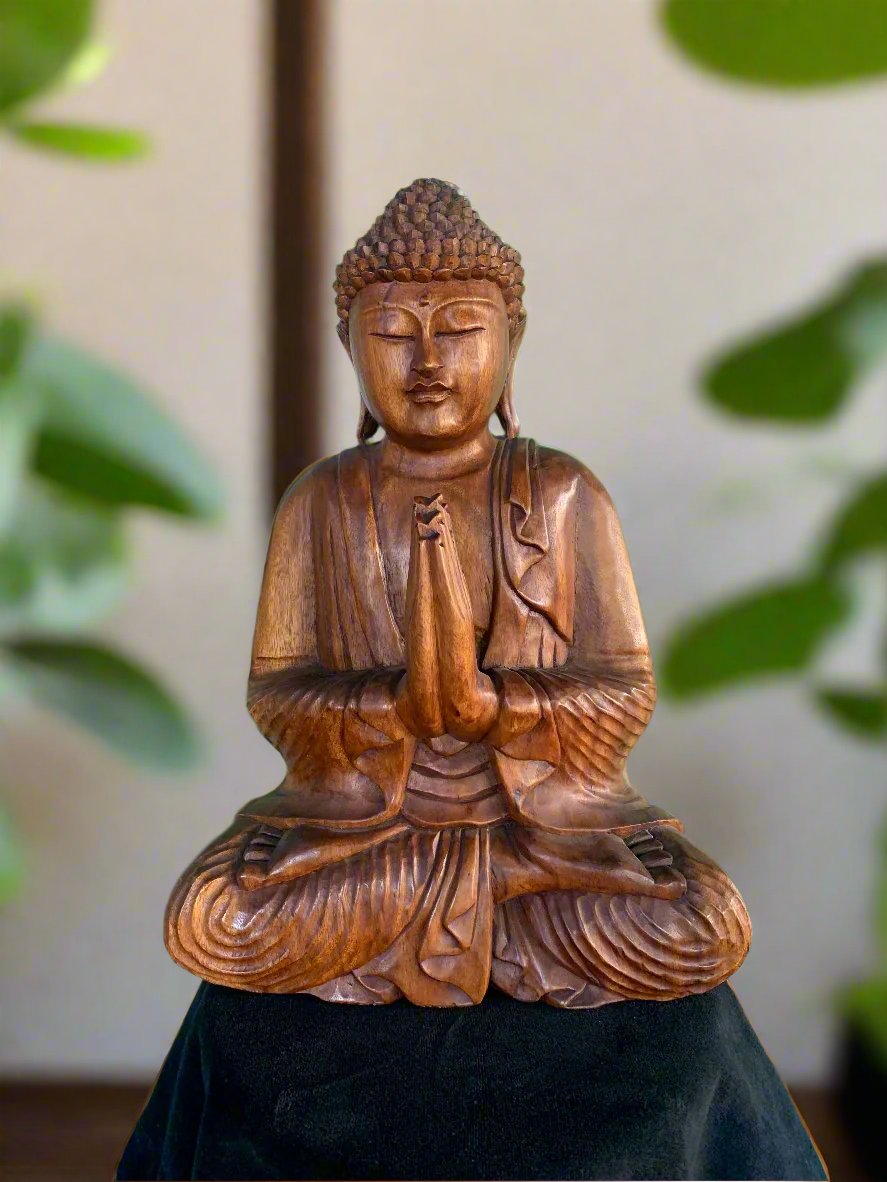 Wooden Buddha statue in meditative praying pose, carved wood with leafy background