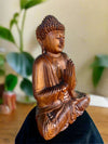 Wooden Buddha statue in meditation with hands together in prayer