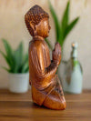 Wooden Buddha statue in a meditative pose with hands in prayer.
