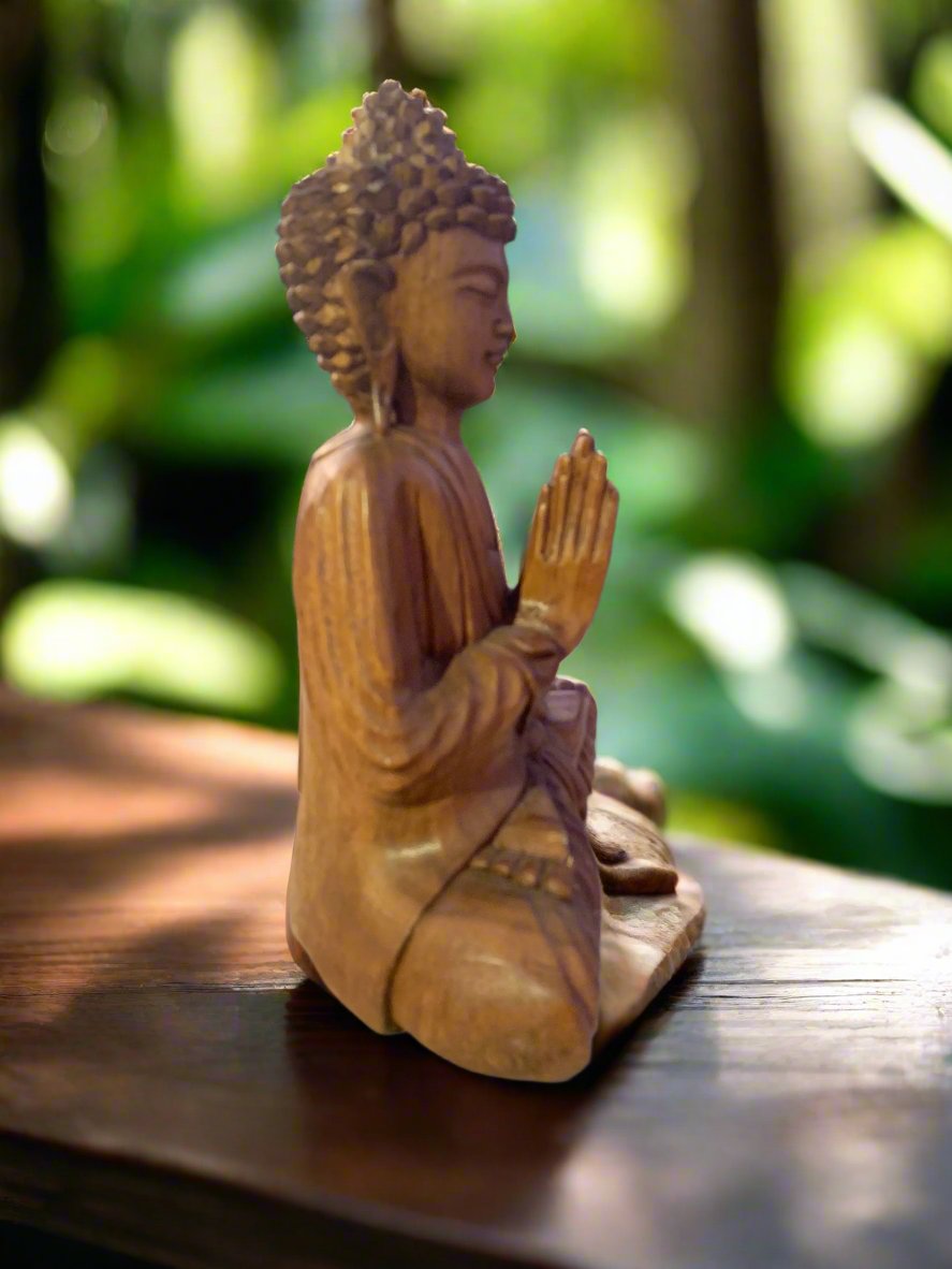 Wooden Buddha statue with hands in prayer on a wooden table, blurred green garden background