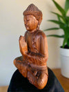 Wooden Buddha statue in a meditative prayer pose with detailed carved robes.