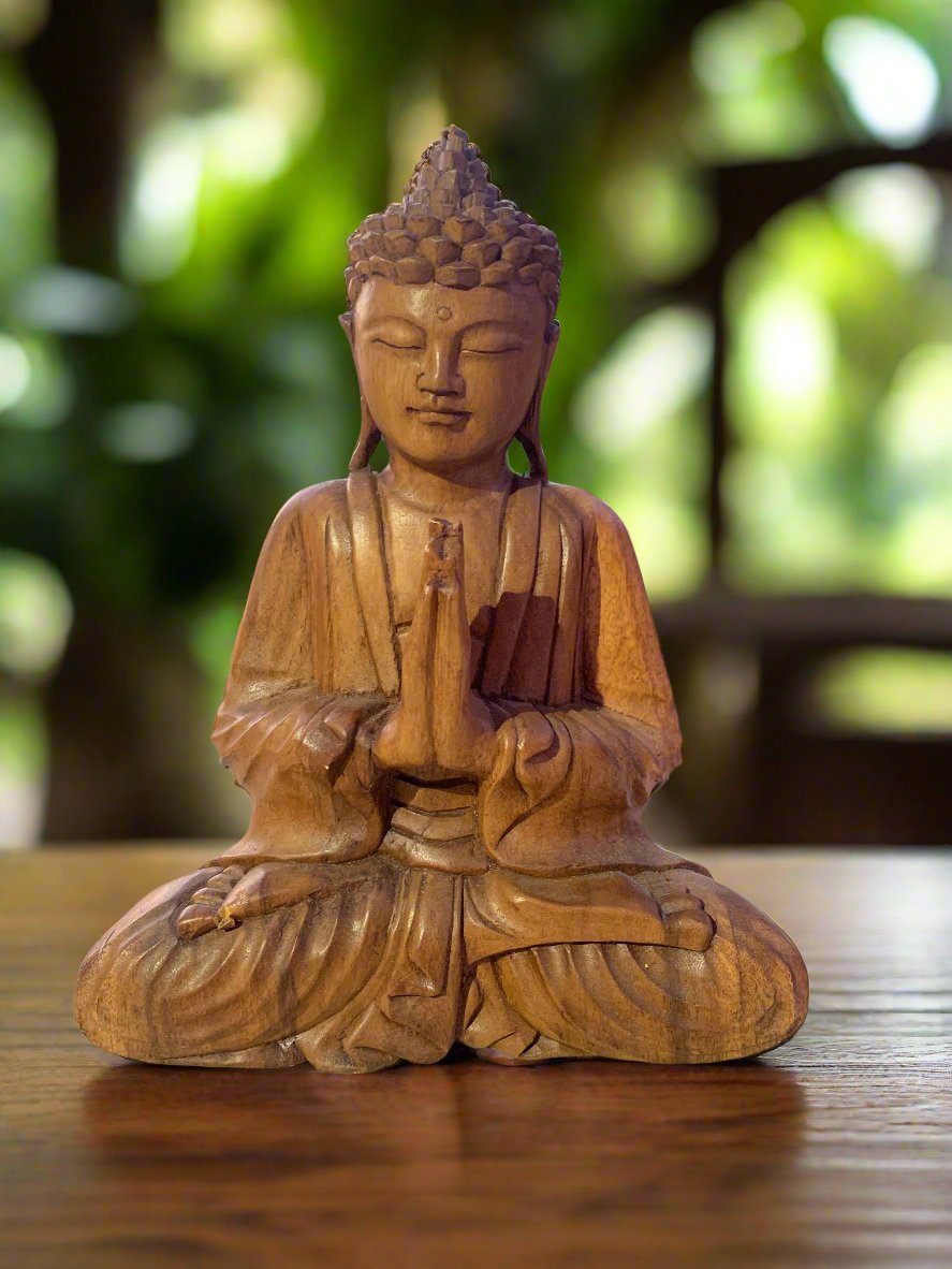 Wooden Buddha statue in a meditative prayer pose on a wooden table with a blurred green background