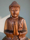 Wooden Buddha statue in a prayer pose with hands pressed together