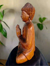 Side-view wooden Buddha statue with hands in prayer