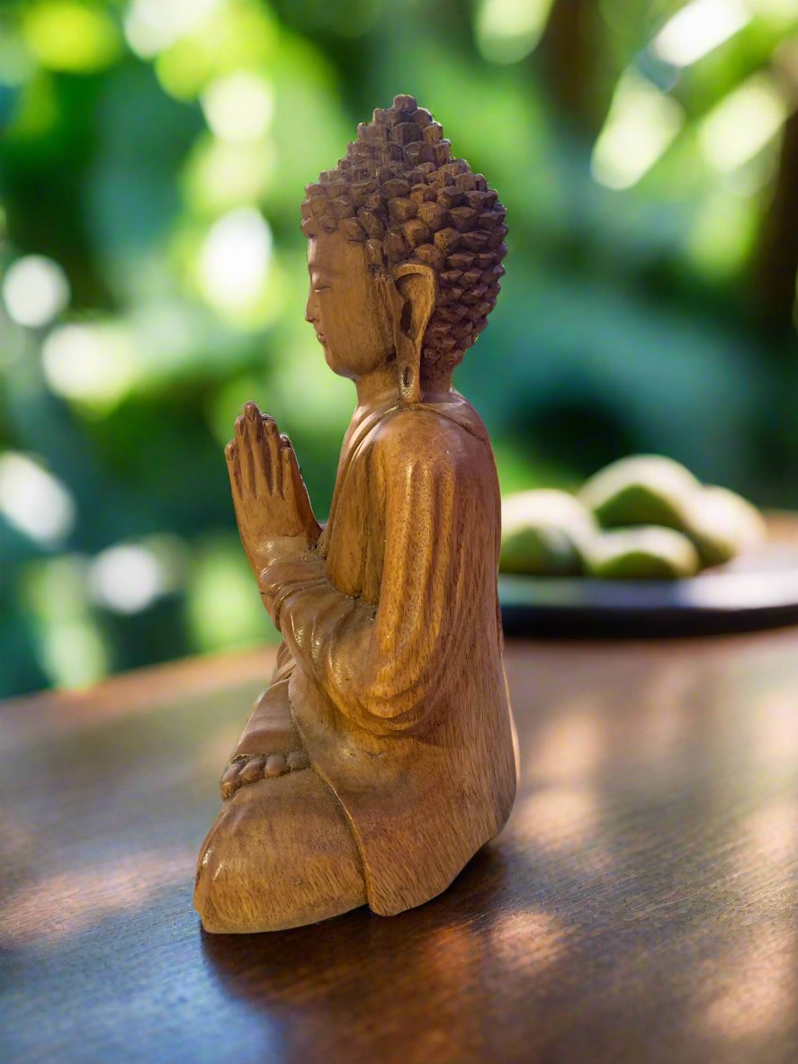 Wooden Buddha statue in a kneeling prayer pose on a wooden table.