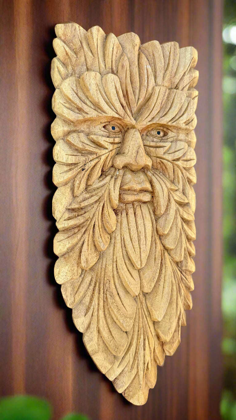 Wooden carved face relief with leaf-shaped patterns forming a beard on a wall plaque.