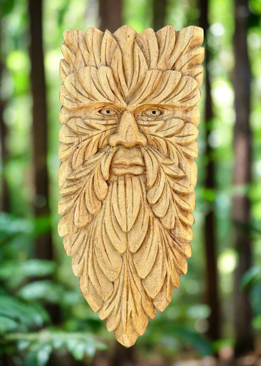 Wooden carved face mask with leaf-patterns resembling a beard in a forest setting