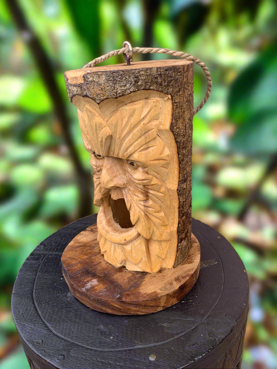 carved wooden face sculpture on a log with a rope handle in a green forest setting