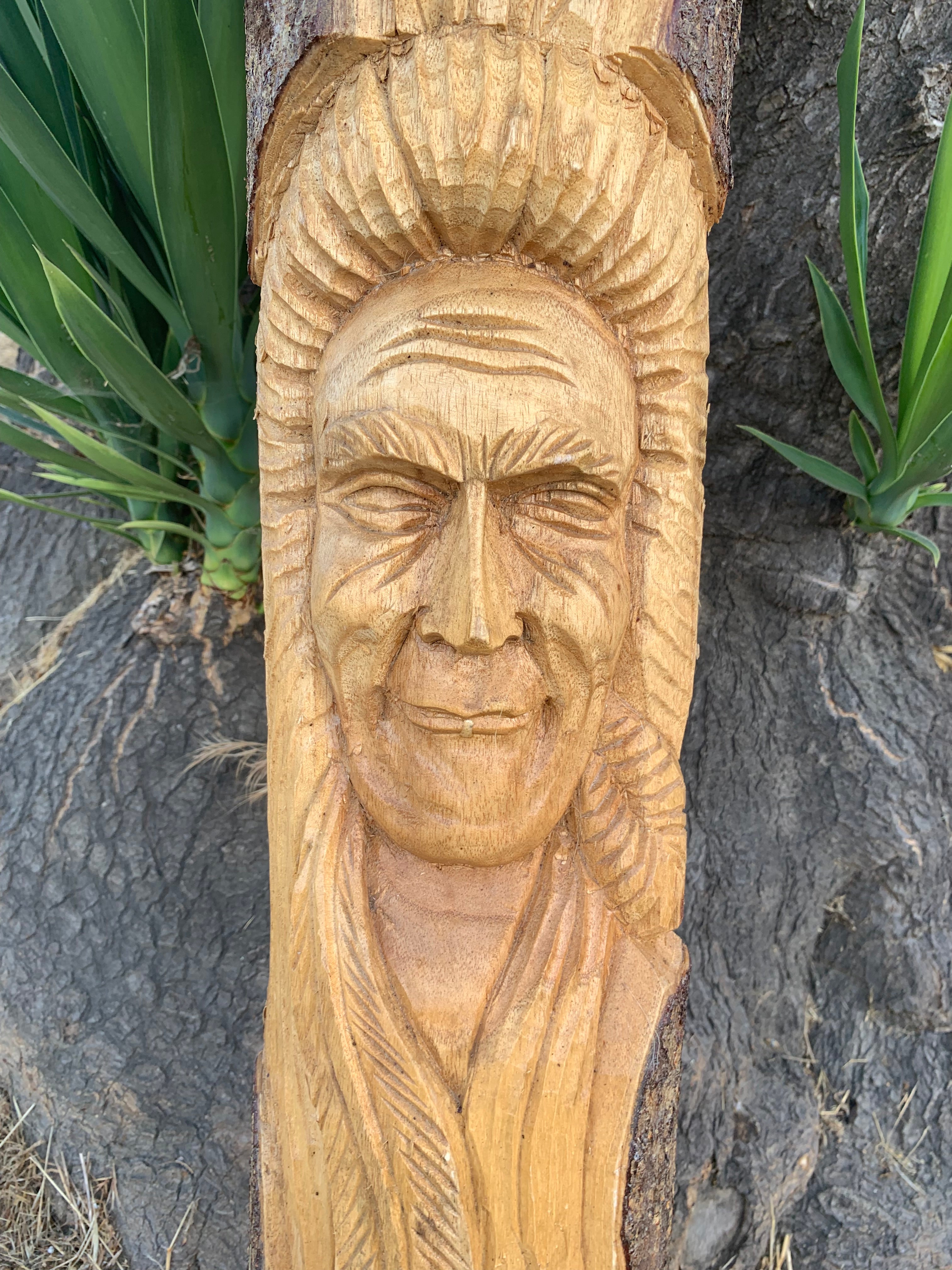 Wooden carved face on a tree trunk with a feathered headdress.
