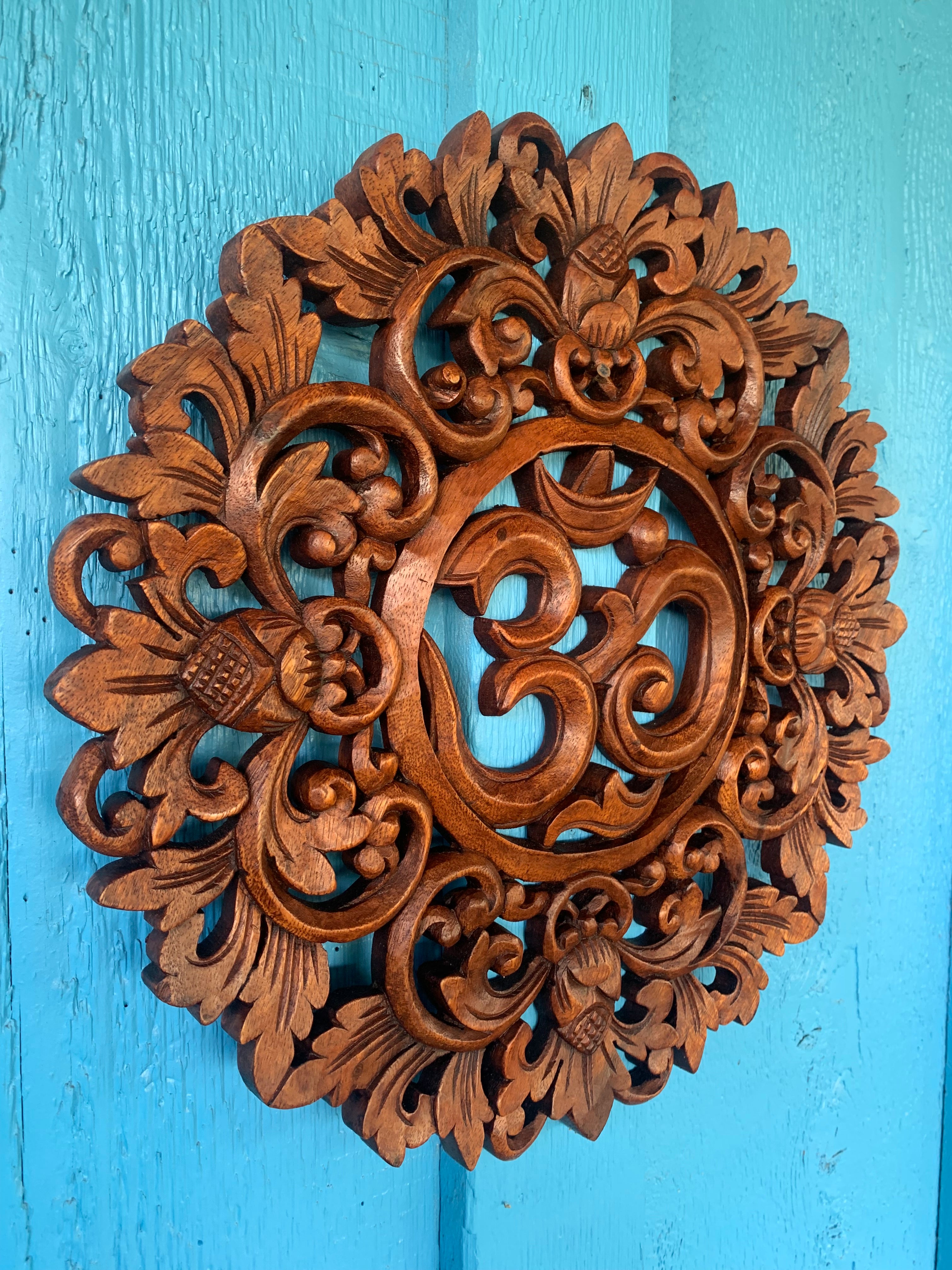 Intricately carved wooden round medallion with floral and scroll designs on a turquoise blue background.