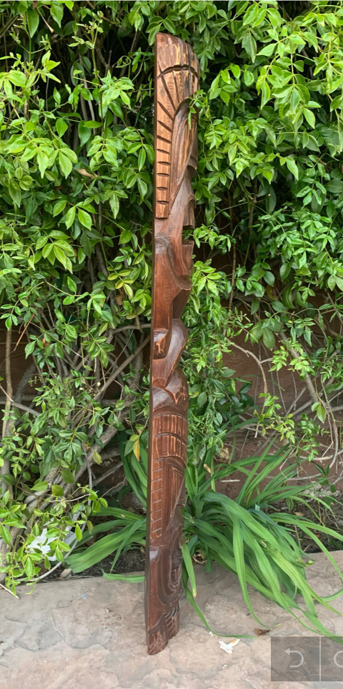 Carved wooden totem pole with geometric patterns against green foliage