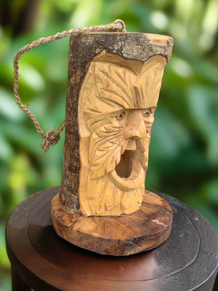 Carved wooden face mask on a tree trunk with rope handle, tiki-style rustic carving