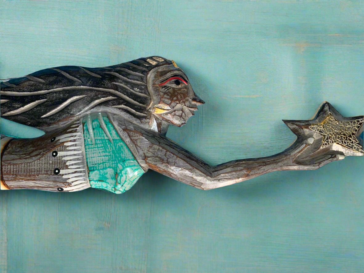 wooden carved woman reaching for a star against a teal background