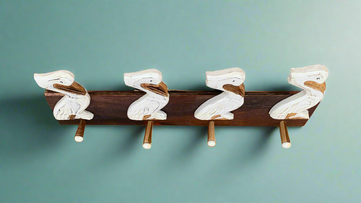 Four white carved wooden ducks perched on a dark wooden beam against a teal wall.