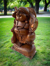 Wooden laughing Buddha statue in a park with lush green grass and trees.