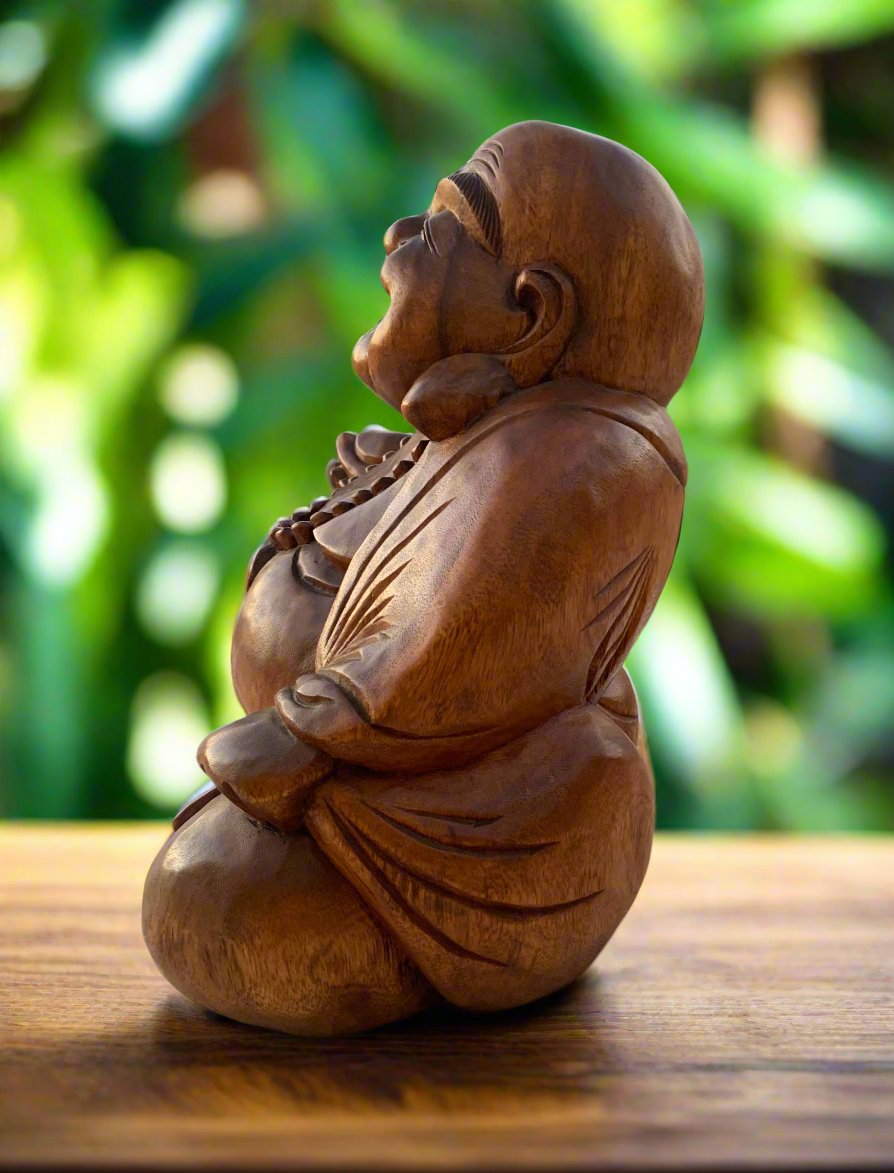 Wooden carved meditating Buddha statue on a table with a lush green background