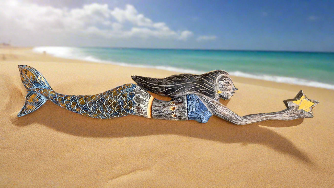 Wooden mermaid figurine on a sandy beach reaching for a yellow star