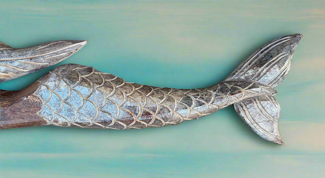 Carved wooden mermaid tail with scale pattern on teal background.
