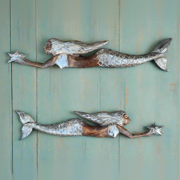 Two wooden mermaid sculptures reaching for stars against a green wooden wall