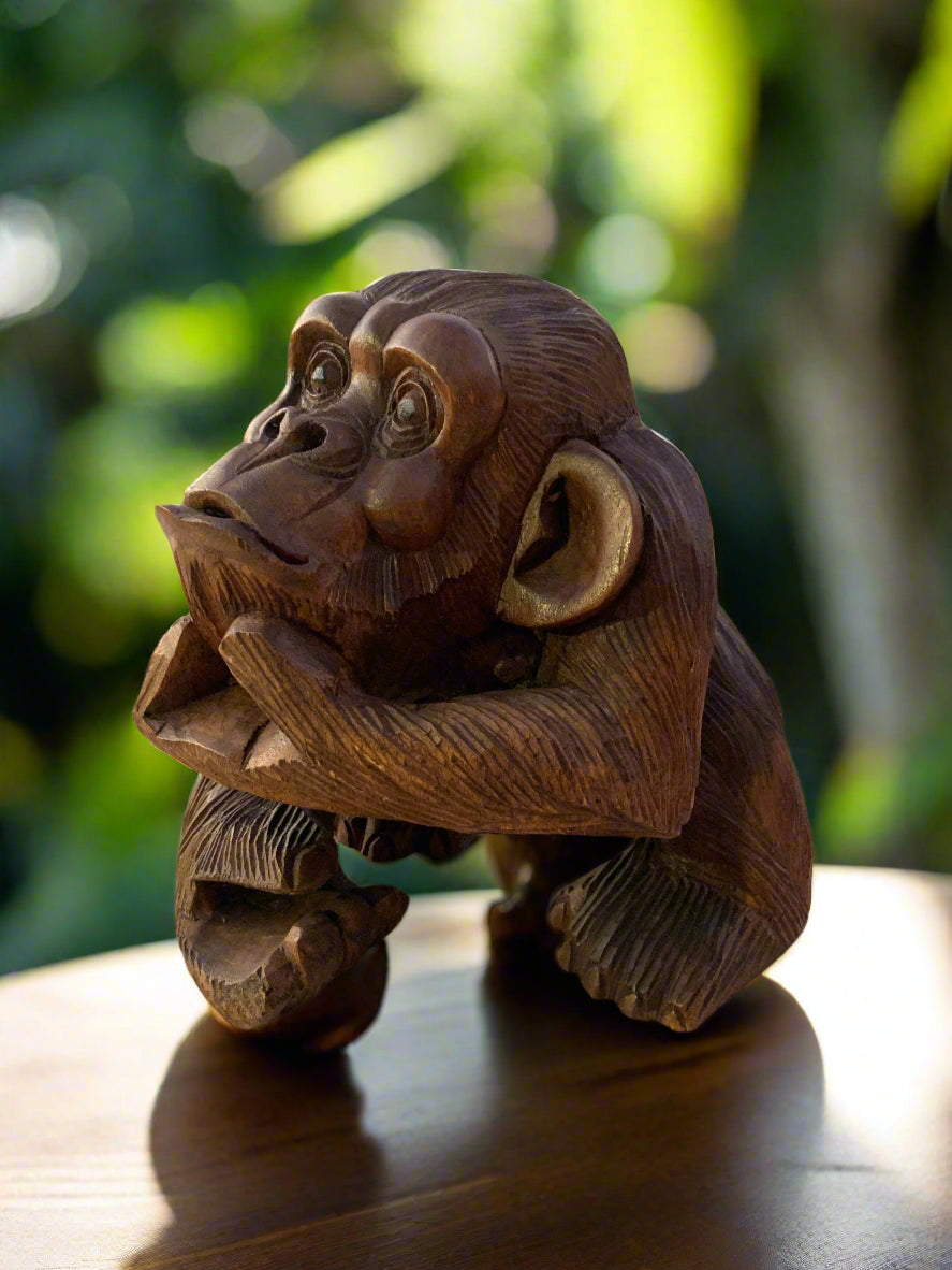 Carved wooden monkey statue on a table with a blurred green garden background