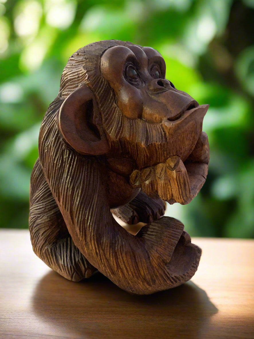 Carved wooden monkey statue in a thinking pose on a table with a green blurred background