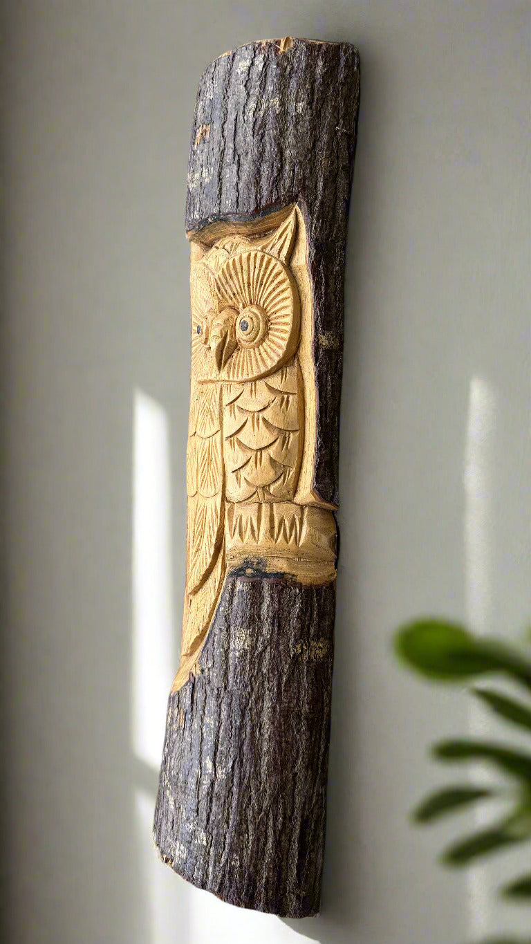 Carved wooden owl perched on a dark tree-log with textured bark.