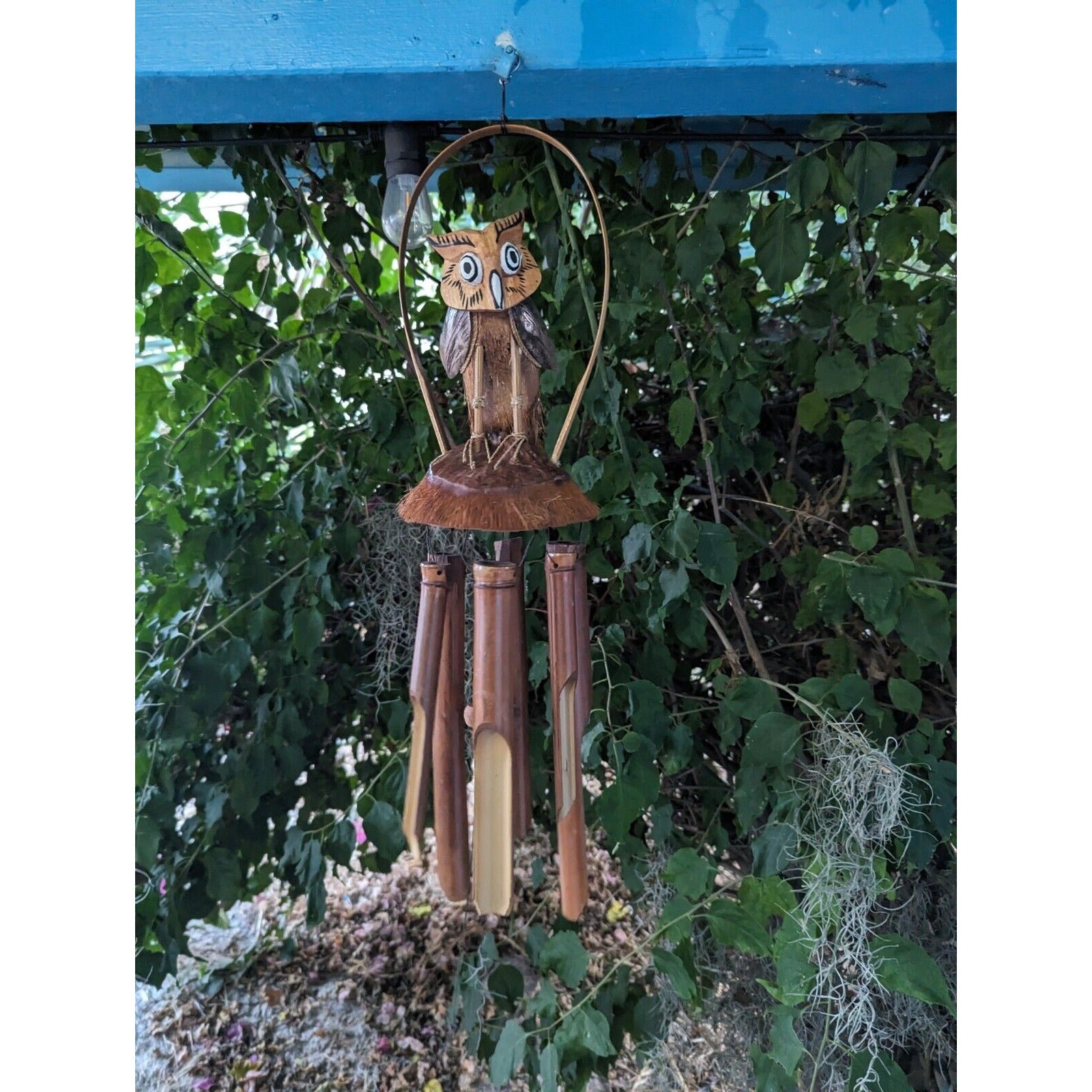 Wooden owl wind chime with bamboo tubes hanging outdoors among green leaves