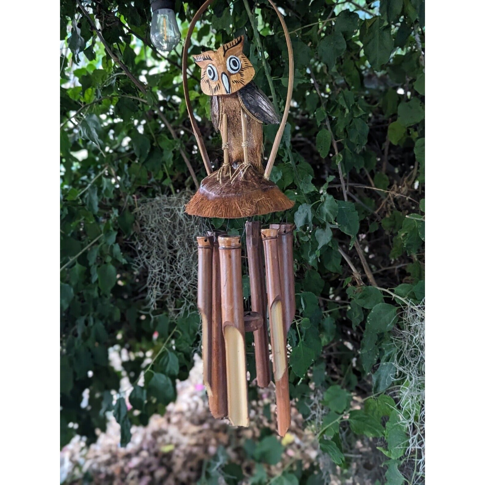 wooden owl wind chime hanging from a tree among green leaves
