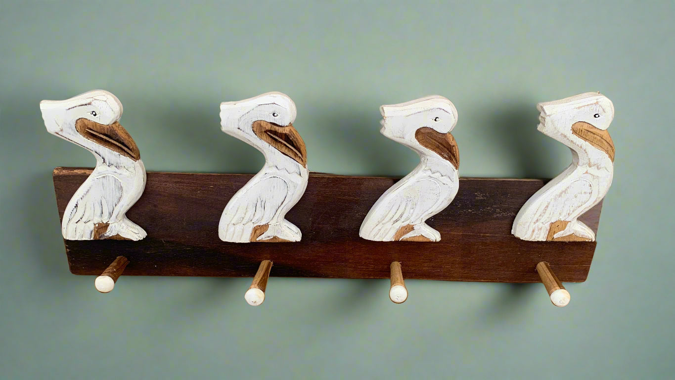 Four white carved pelican figures on a dark wooden coat rack