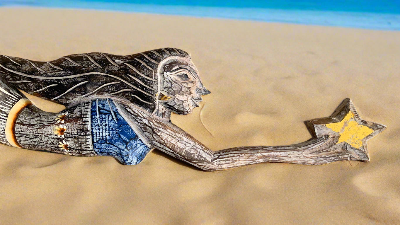 Wooden carved girl reaching for a yellow star on a sandy beach with blue waves in the background
