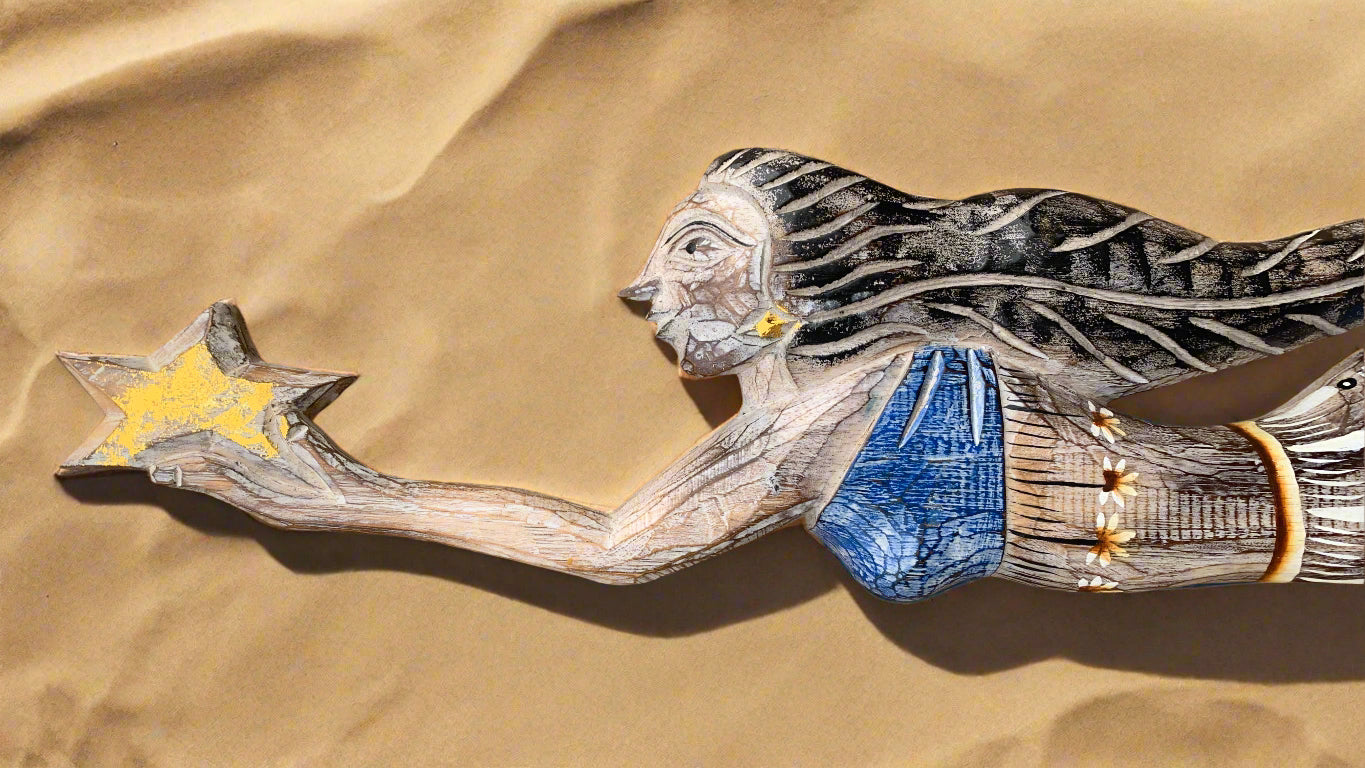 Wooden carved woman in blue dress reaching for a yellow star on sandy background