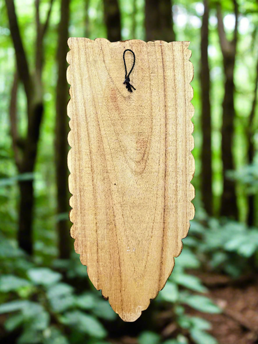 wooden tag with scalloped edges hanging by a cord in a green forest