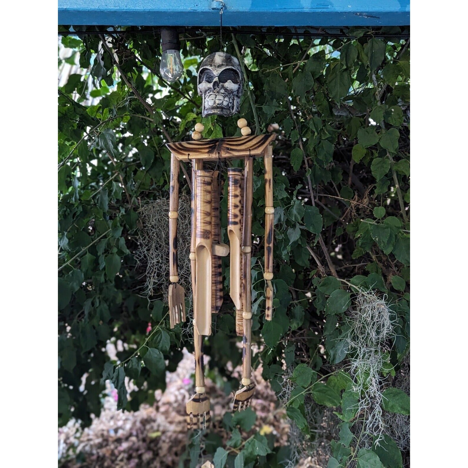 Wooden skeleton wind chime hanging in a garden among green leaves, Halloween decor