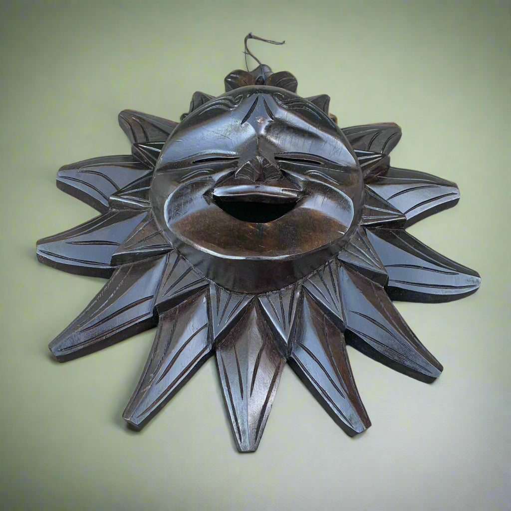 Dark wooden sun mask with a carved laughing face