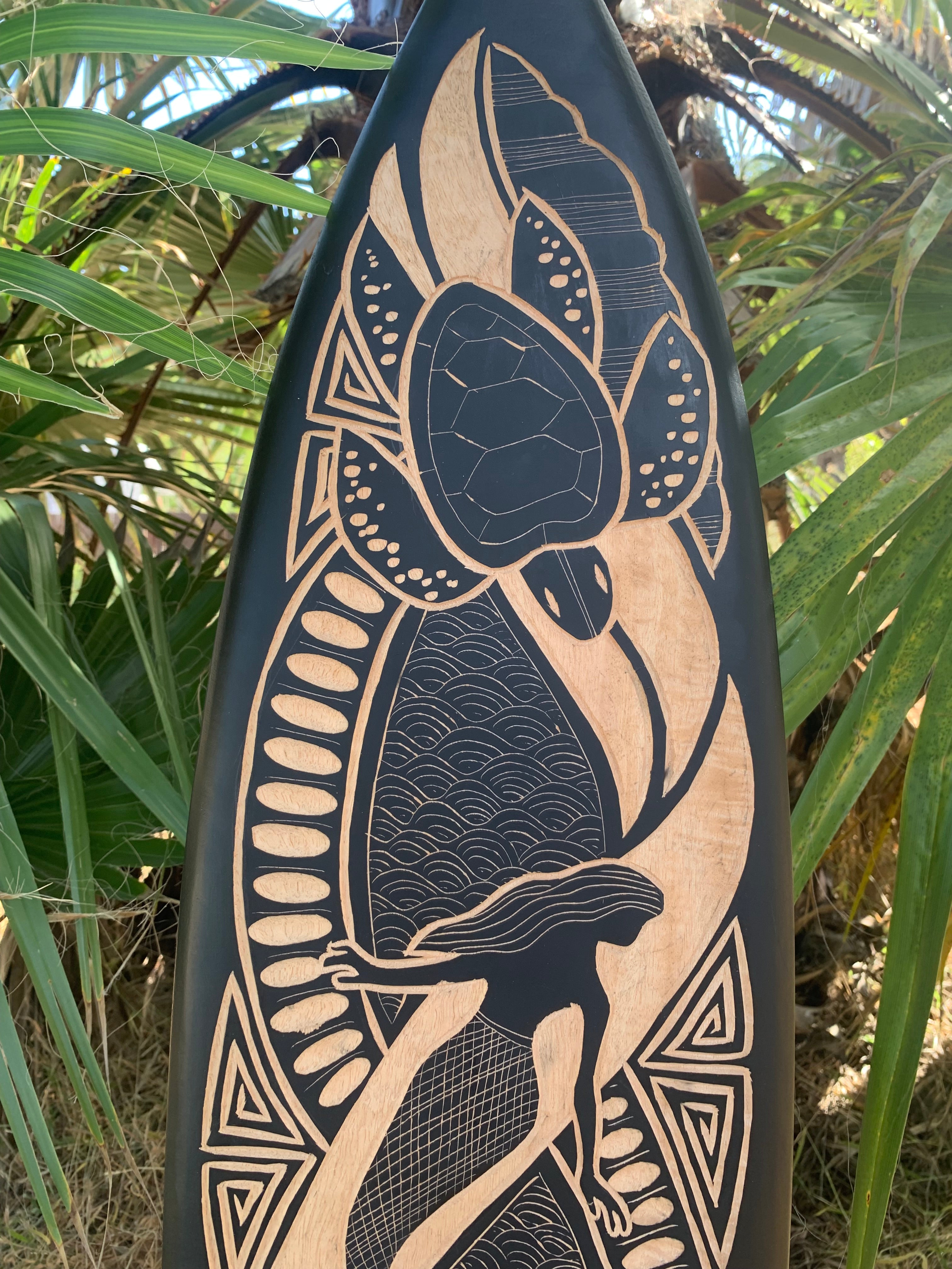 Carved wooden surfboard featuring a stylized woman, flowing hair, waves, and a large floral motif.