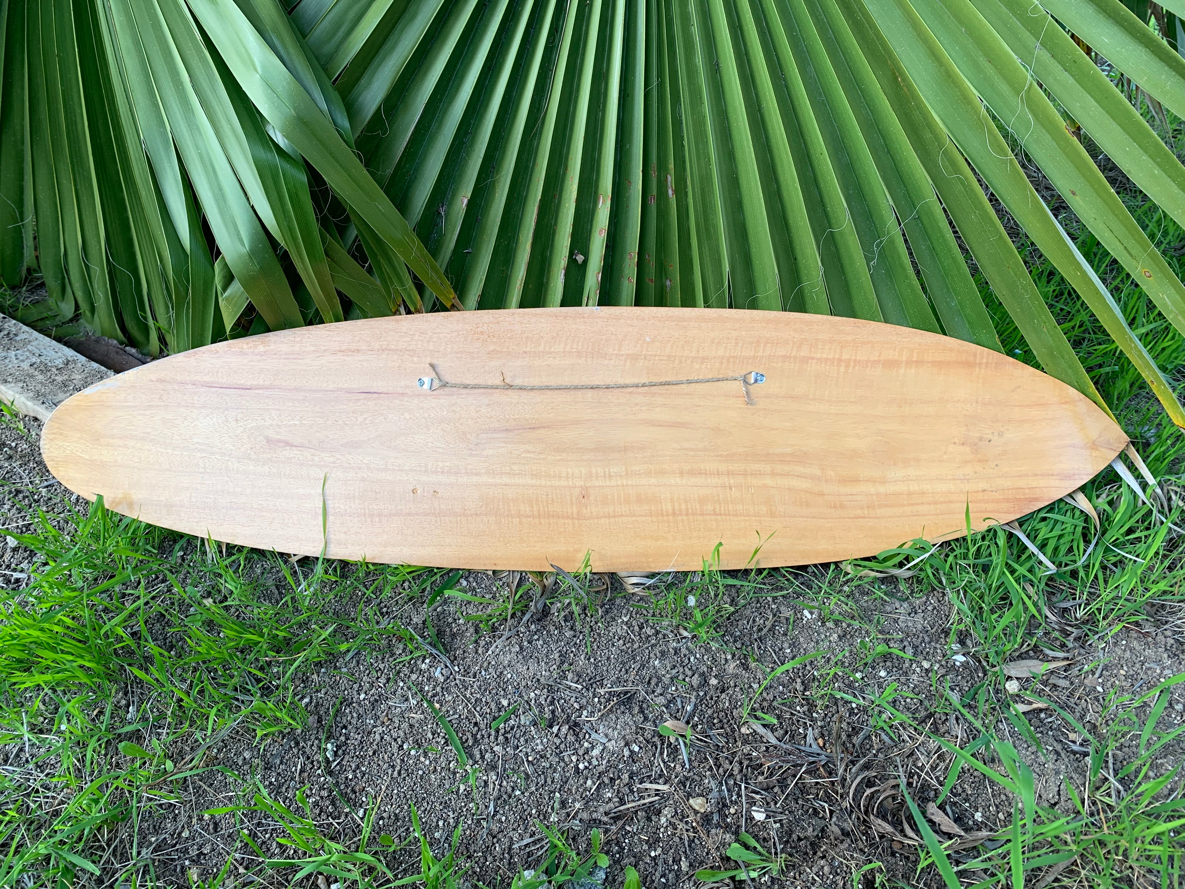 Wooden surfboard lying on dirt and grass with large green palm fronds in the background