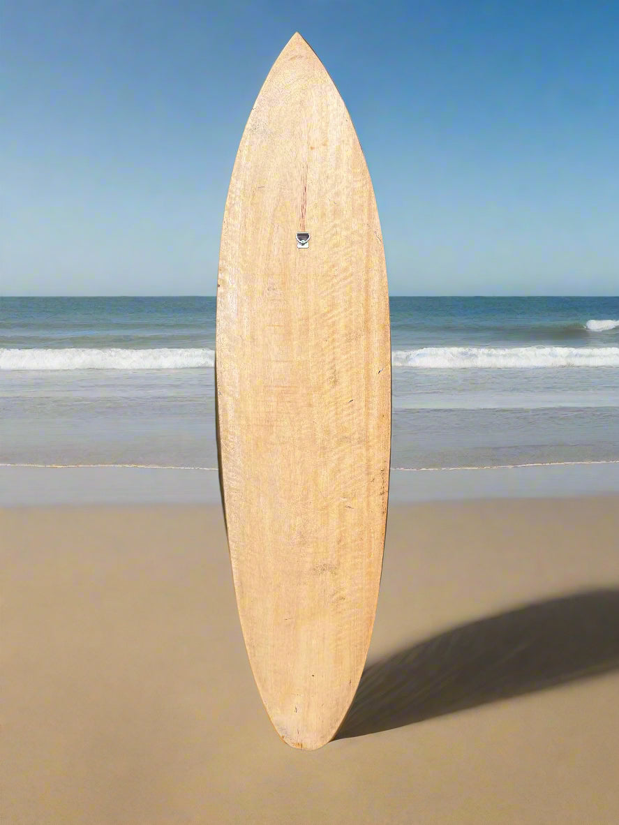 Wooden surfboard standing upright on a sandy beach with the ocean in the background