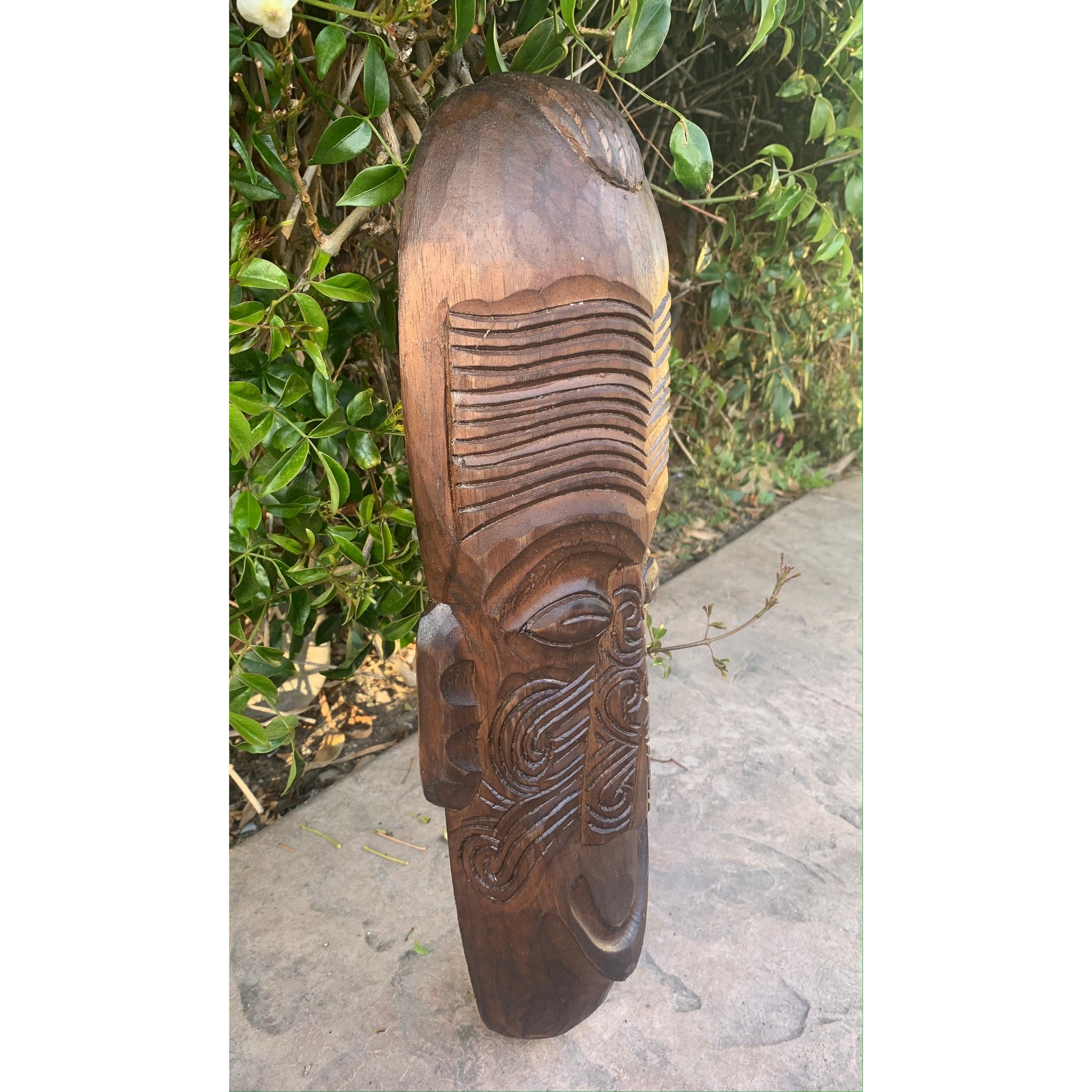 Hand-carved wooden tiki statue with facial features and decorative forehead lines outdoors.