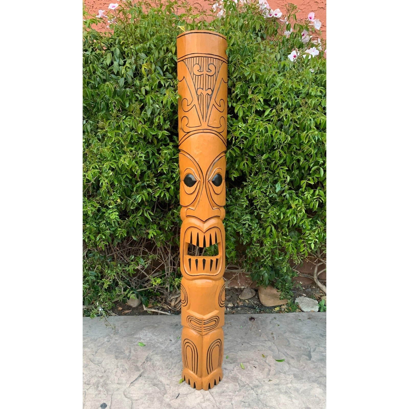 Tall carved wooden tiki pole with stylized faces in a garden setting.