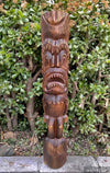 carved wooden tiki statue with an open mouth and sharp teeth in front of green shrubs