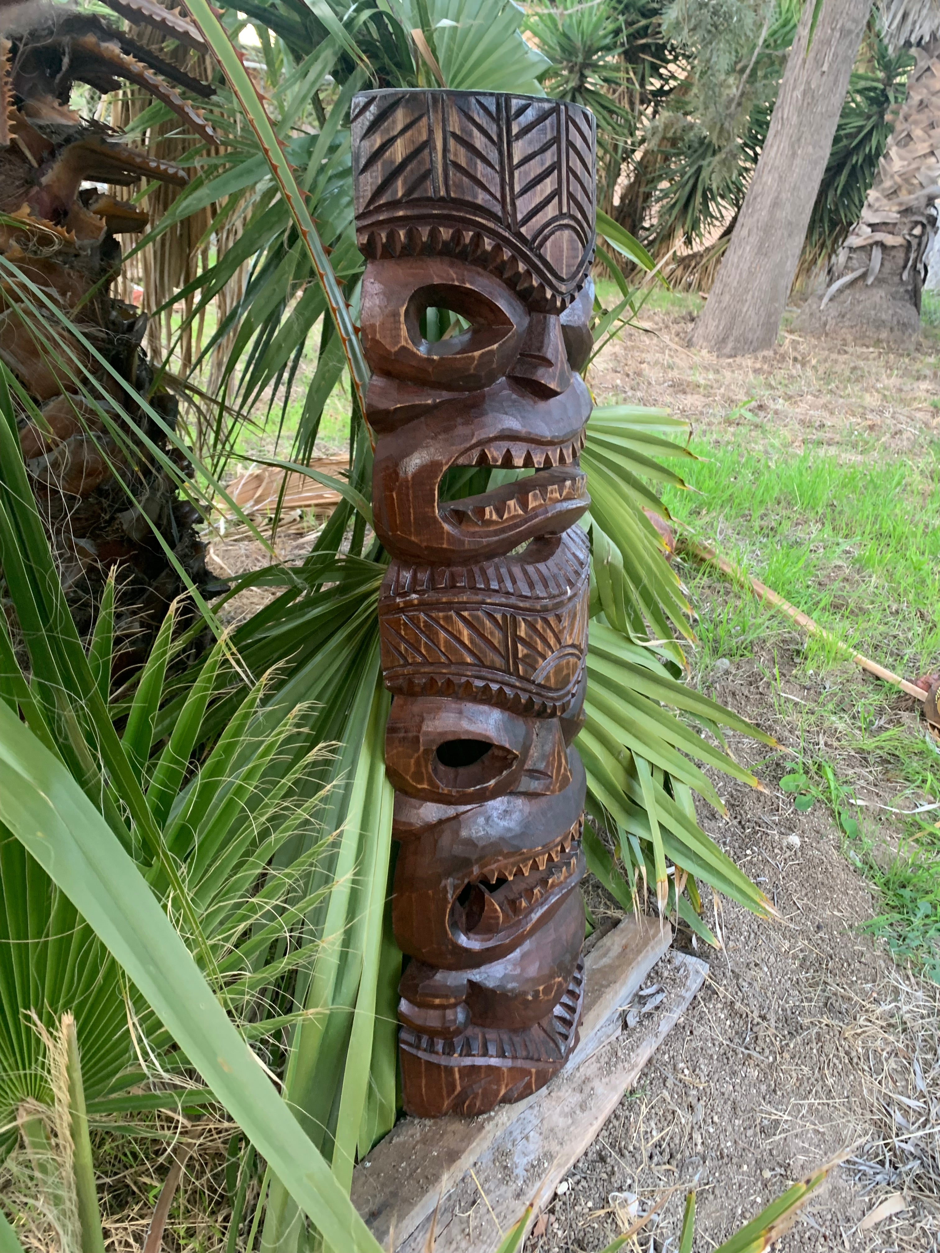 Tall carved wooden tiki totem with stacked faces in an outdoor garden