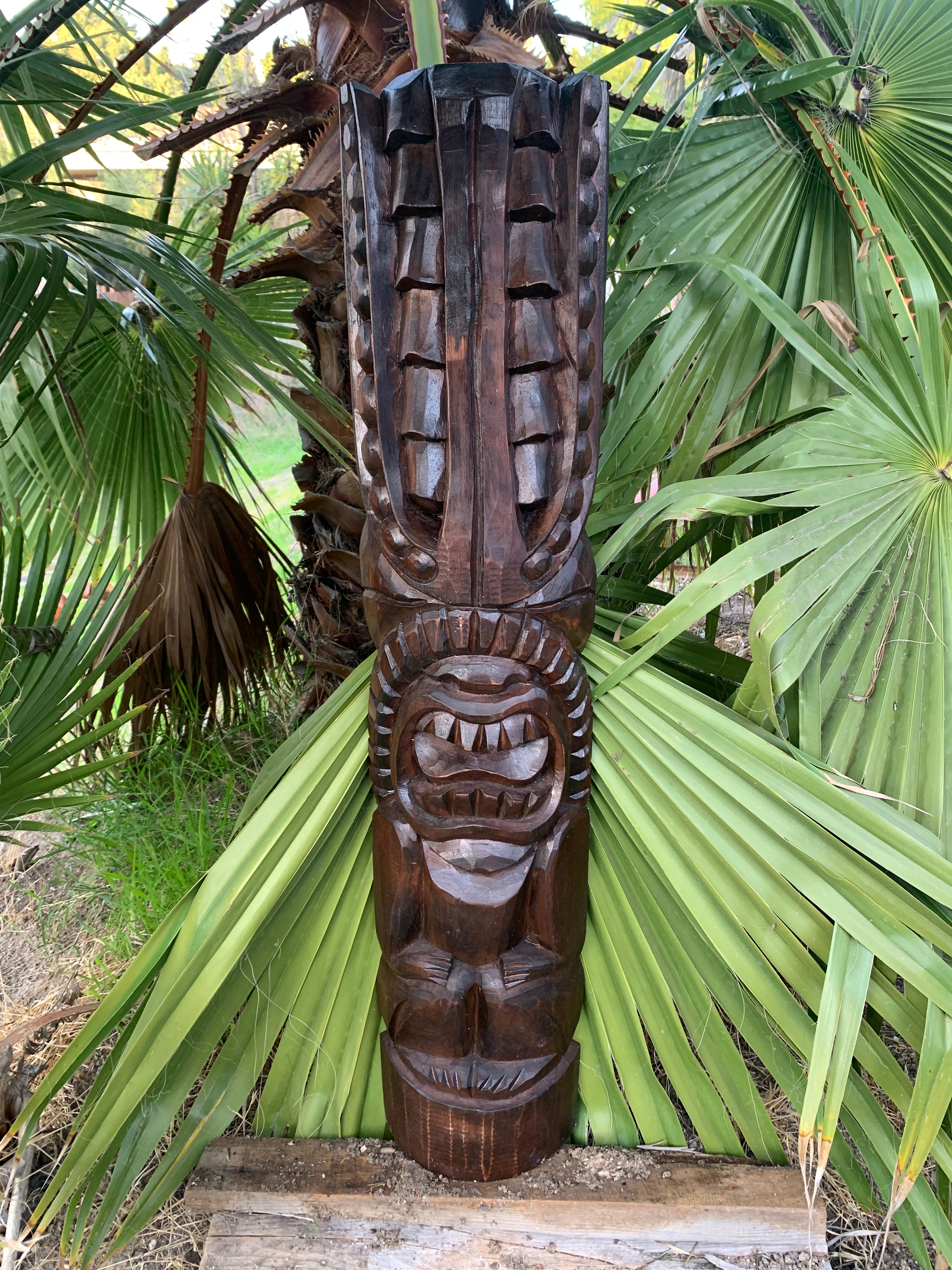 Dark wooden tiki totem carving among green palm leaves