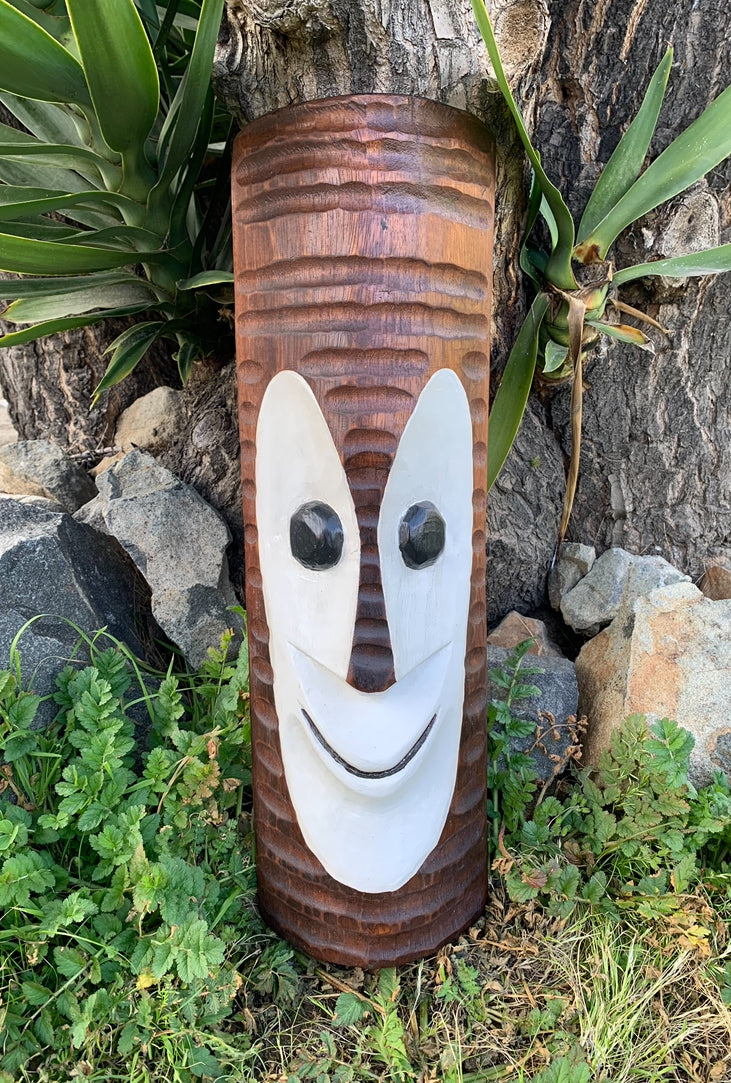 carved wooden tiki totem with a white smiling face and black eyes