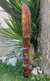 Carved wooden totem pole with a stylized face and feather-like patterns outdoors