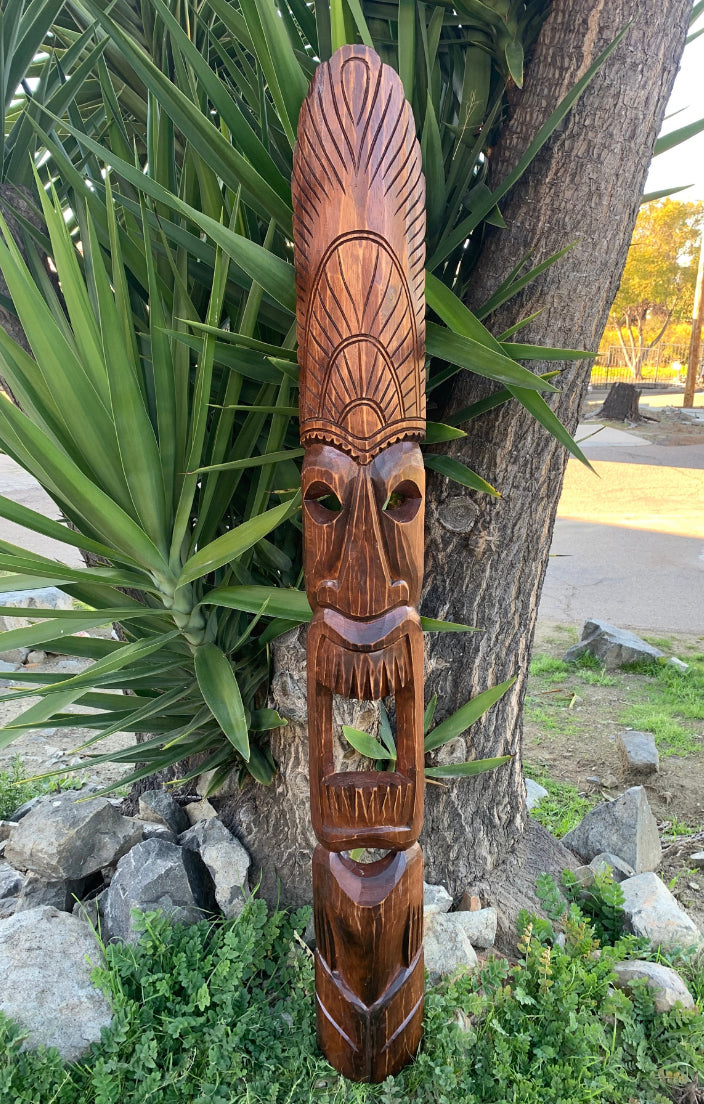Outdoor wooden totem pole carving with a face and geometric patterns in a garden setting