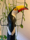 Wooden toucan sculpture with yellow beak among green vines