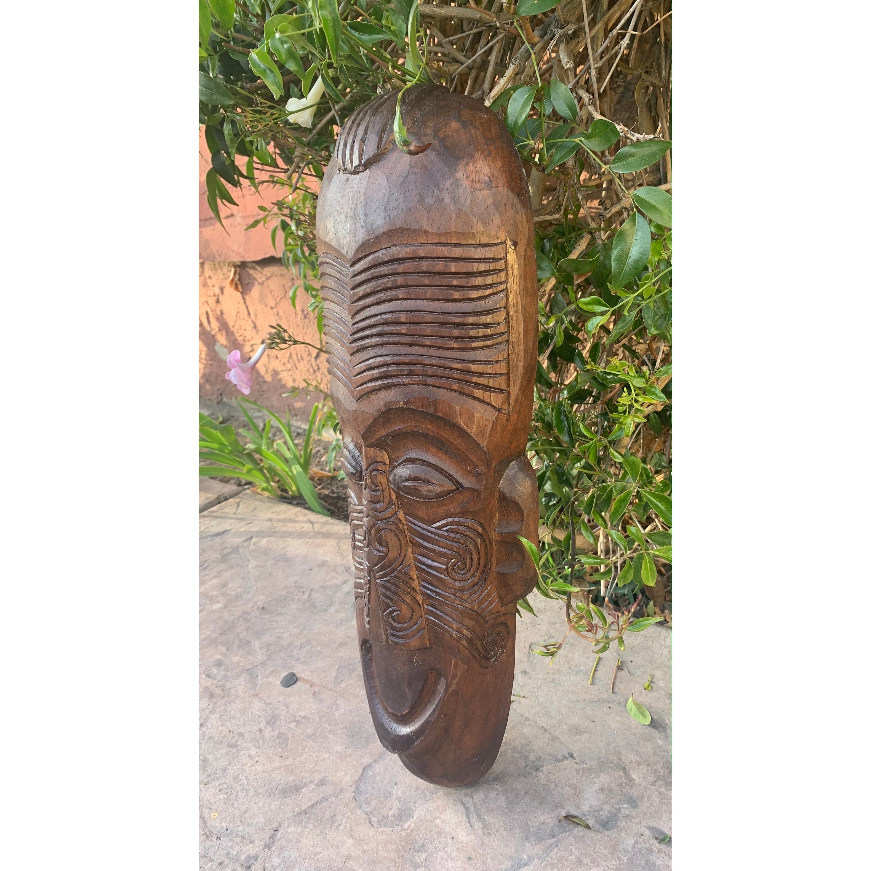 Tall carved wooden tribal mask with geometric patterns in a garden