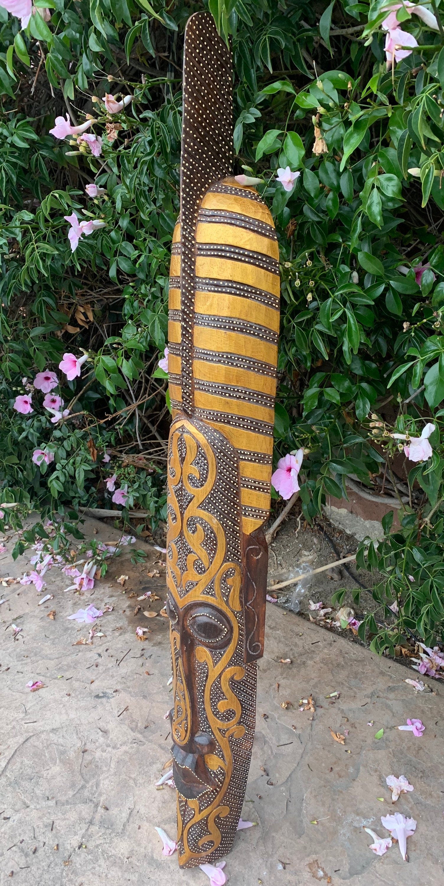 Aboriginal-style carved wooden staff with dotted stripes and swirling motifs against green foliage