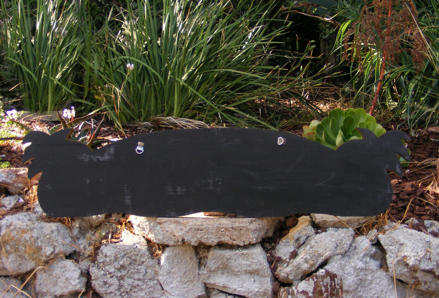 Black chalkboard sign on a stone wall in a garden with green plants